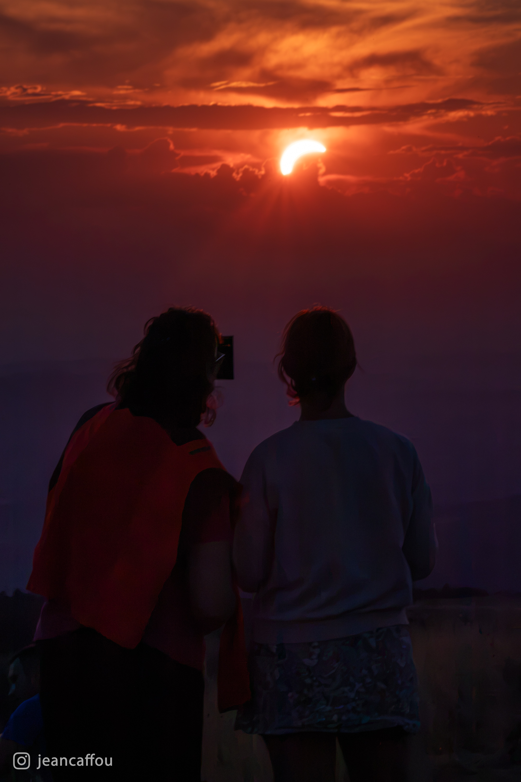 Dve opazovalki, ki skozi večerno meglico opazujeta srpasto Sonce.