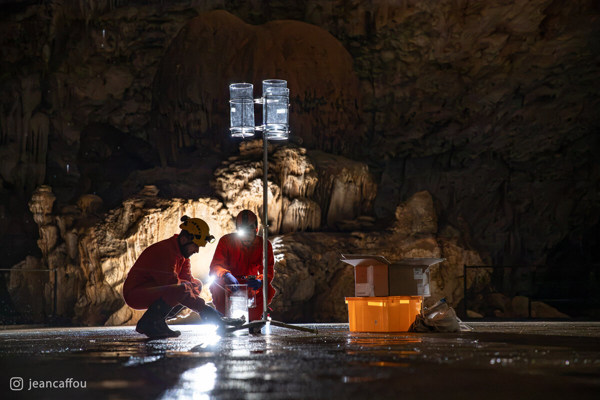 Raffaele Bruschi and Blaž Kogovšek crouch beside a sampling stand, their headlamps lighting the containers on the cave floor in Koncertna dvorana (Concert Hall) in Postojna Cave.