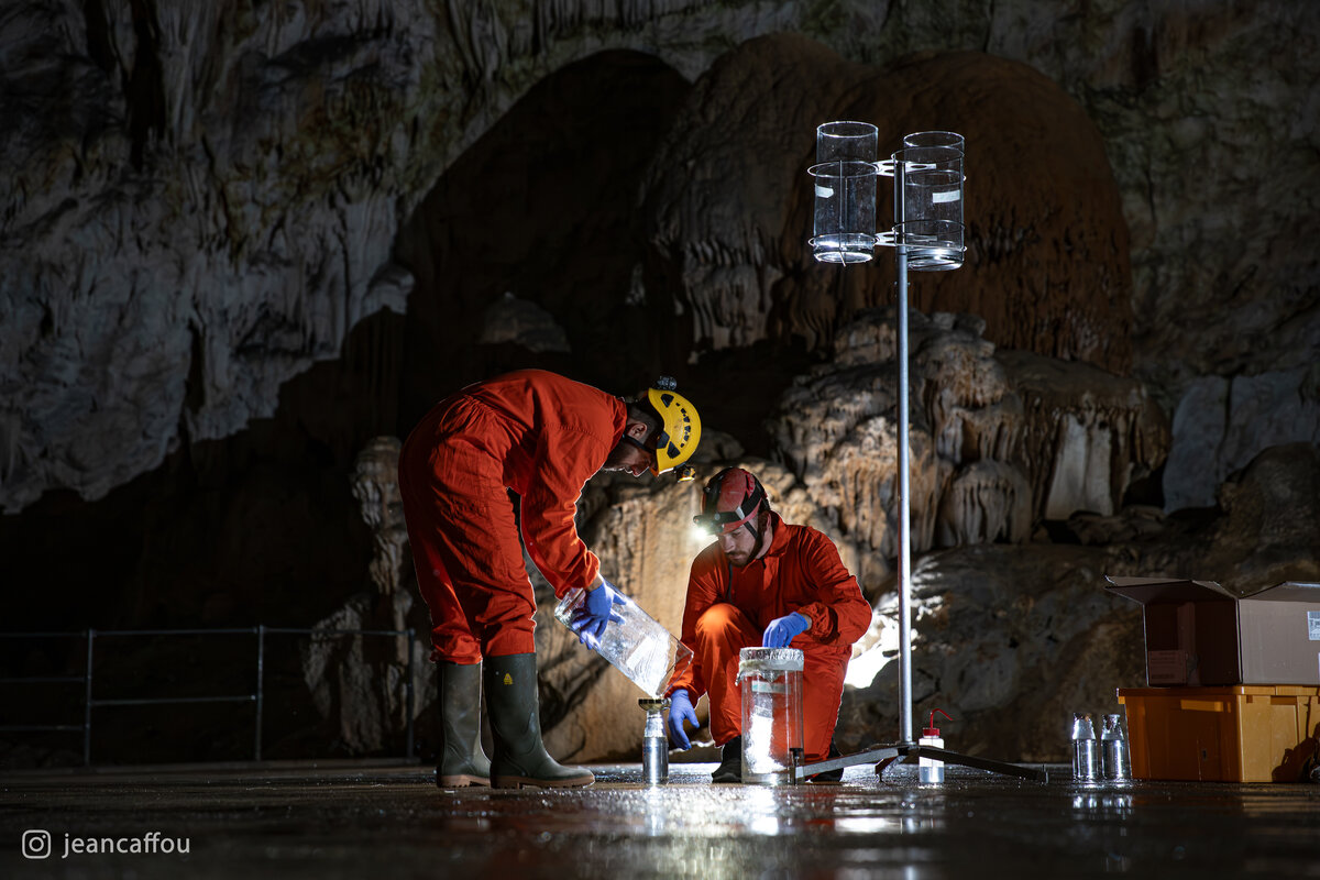 Blaž Kogovšek bends over the glass containers while Raffaele Bruschi handles a sample beneath the raised collectors in Koncertna dvorana (Concert Hall) in Postojna Cave.