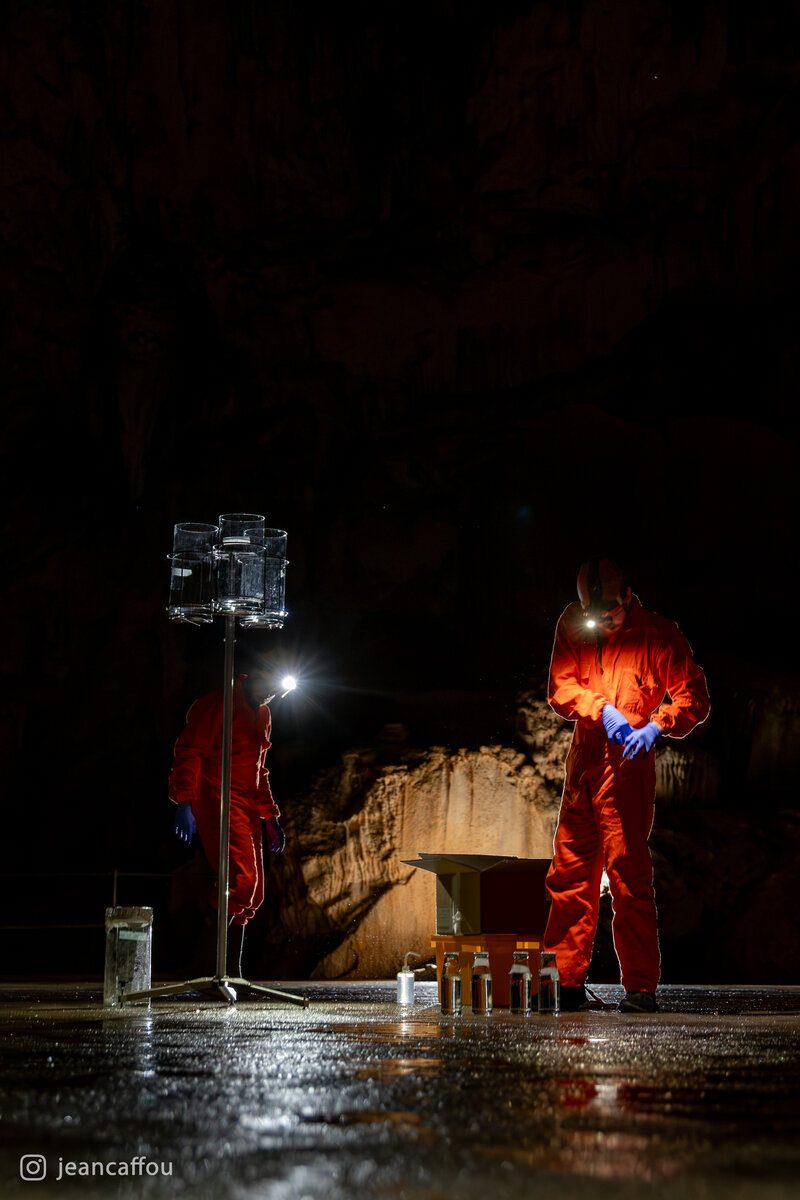 Raffaele Bruschi checks a glass container by headlamp, with sample jars arranged at his feet in the dark Koncertna dvorana (Concert Hall) in Postojna Cave.
