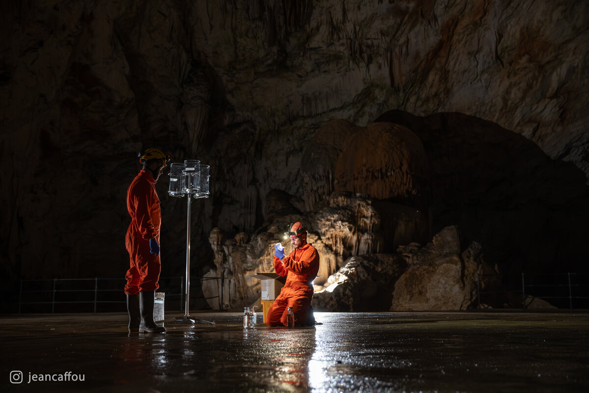 Blaž Kogovšek reaches toward the elevated collectors while Raffaele Bruschi kneels beside the sample containers below a cave wall in Koncertna dvorana (Concert Hall) in Postojna Cave.