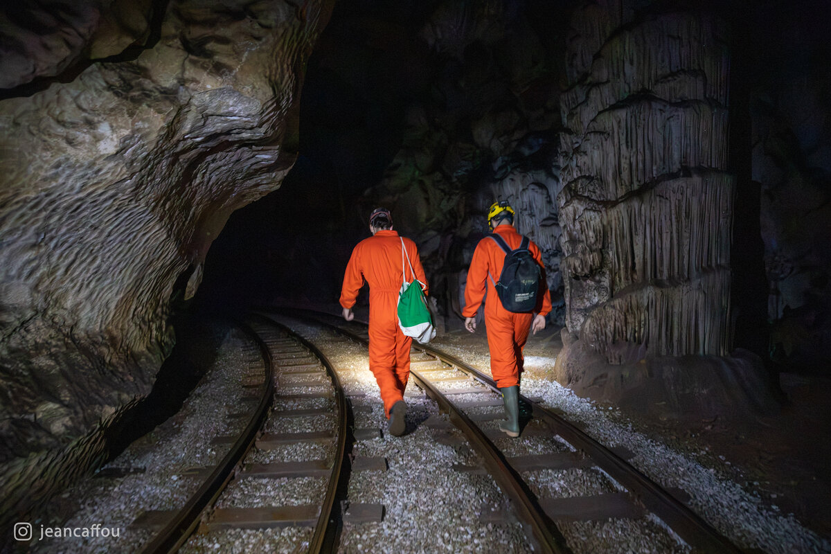 Blaž Kogovšek and Raffaele Bruschi carry equipment along the railway through a narrow, illuminated passage in Postojna Cave.