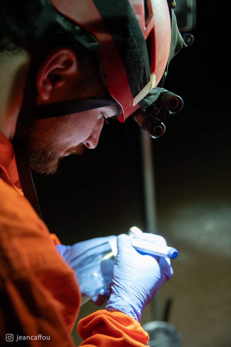 Raffaele Bruschi labels a glass sample container with tape and a marker under his headlamp so the samples can be identified.