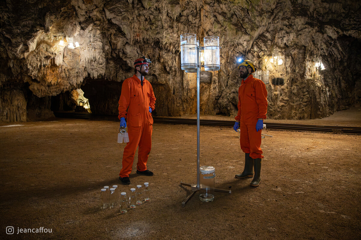 Raffaele Bruschi and Blaž Kogovšek stand on either side of a deposition sampler in Plesna dvorana, with glass jars on the ground.