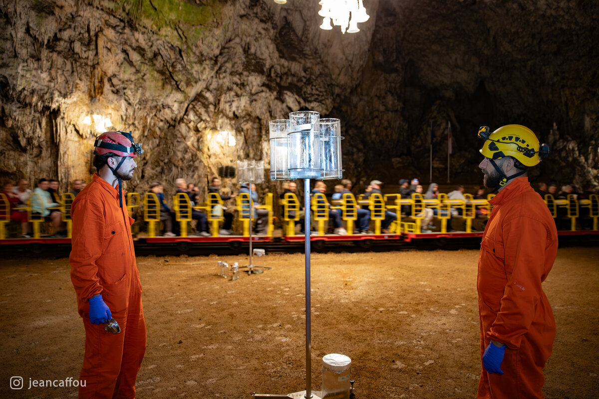 The yellow cave train passes behind Raffaele Bruschi, Blaž Kogovšek and the glass sampling vessels in Plesna dvorana.