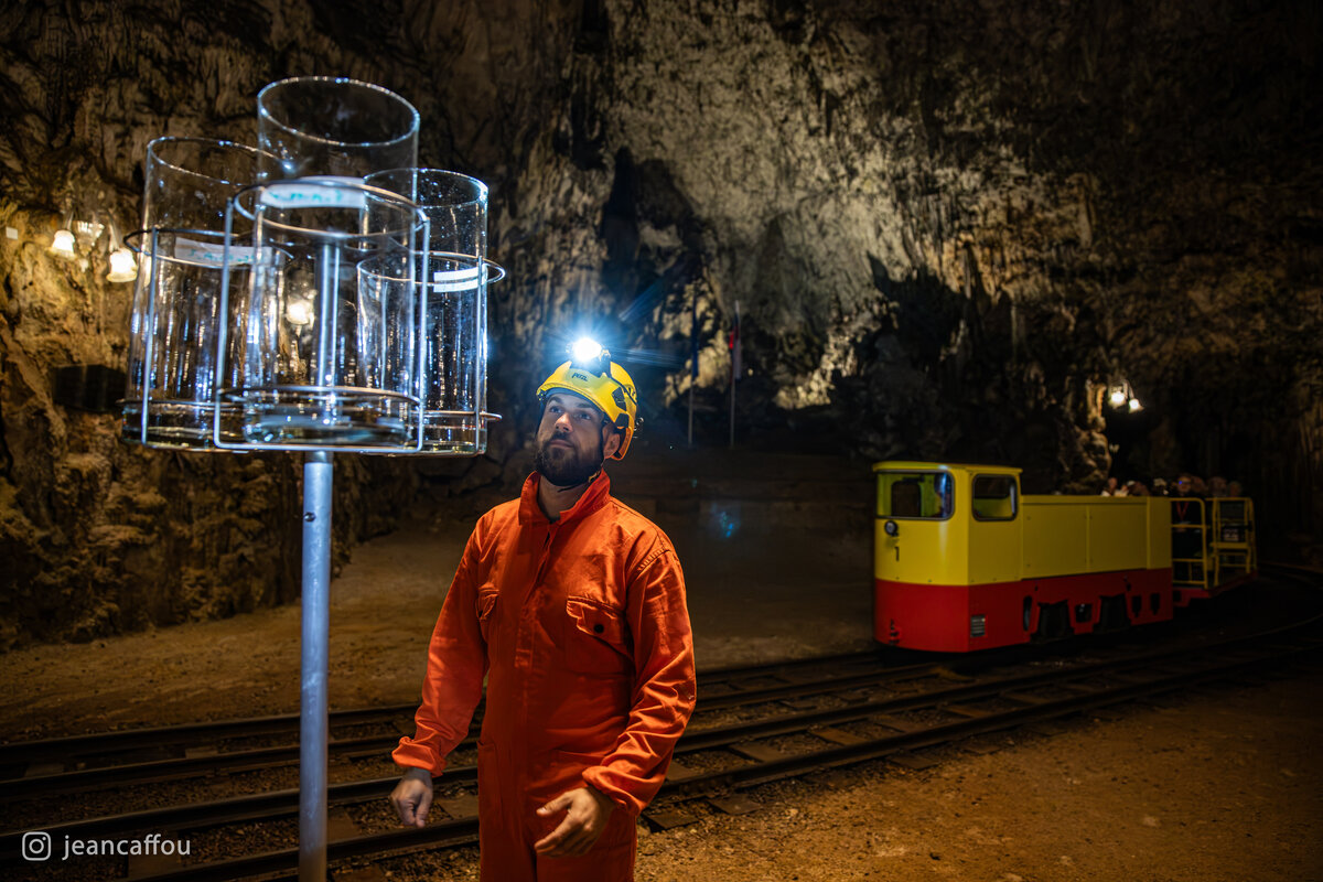Blaž Kogovšek looks toward the elevated glass collectors, his headlamp shining beside the passing train in Plesna dvorana.